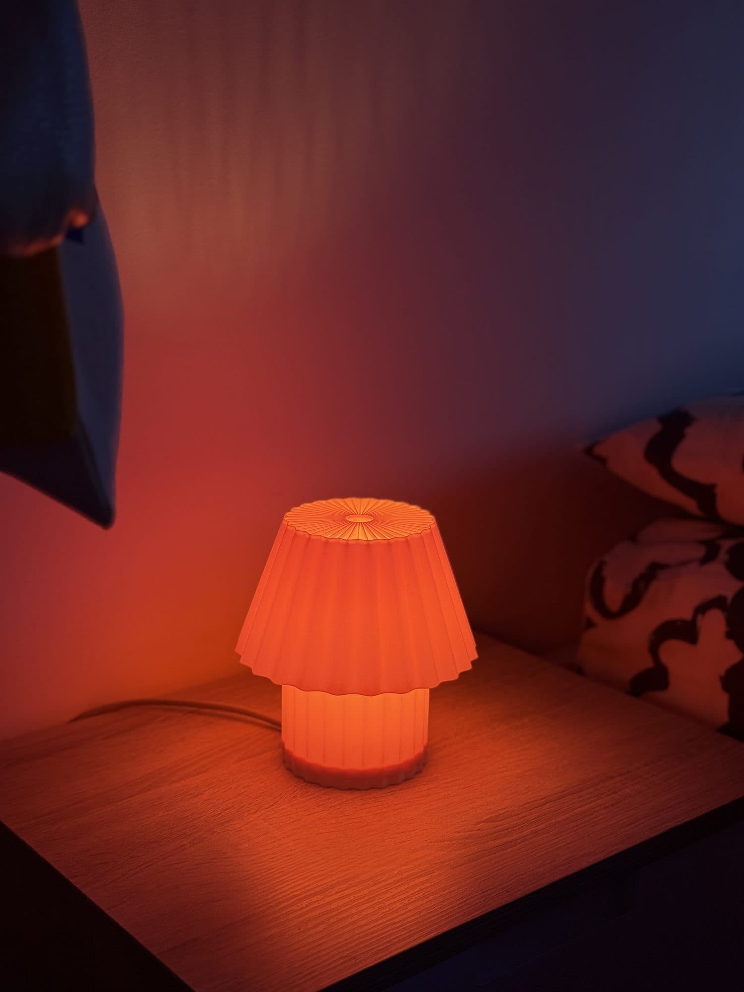 Lámpara Champi encendida sobre una mesa de noche de madera, con luz naranja